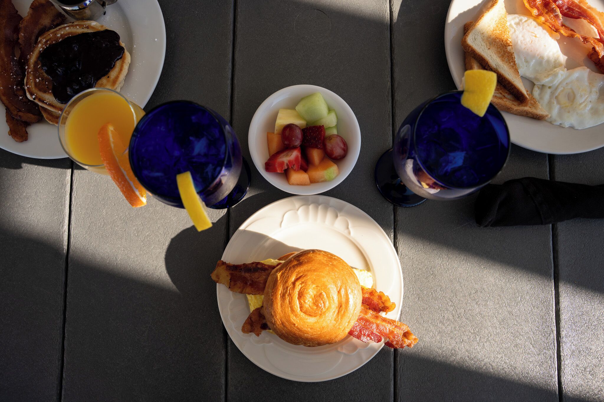 A breakfast setting with toast, eggs, bacon, and a fruit bowl on a table.