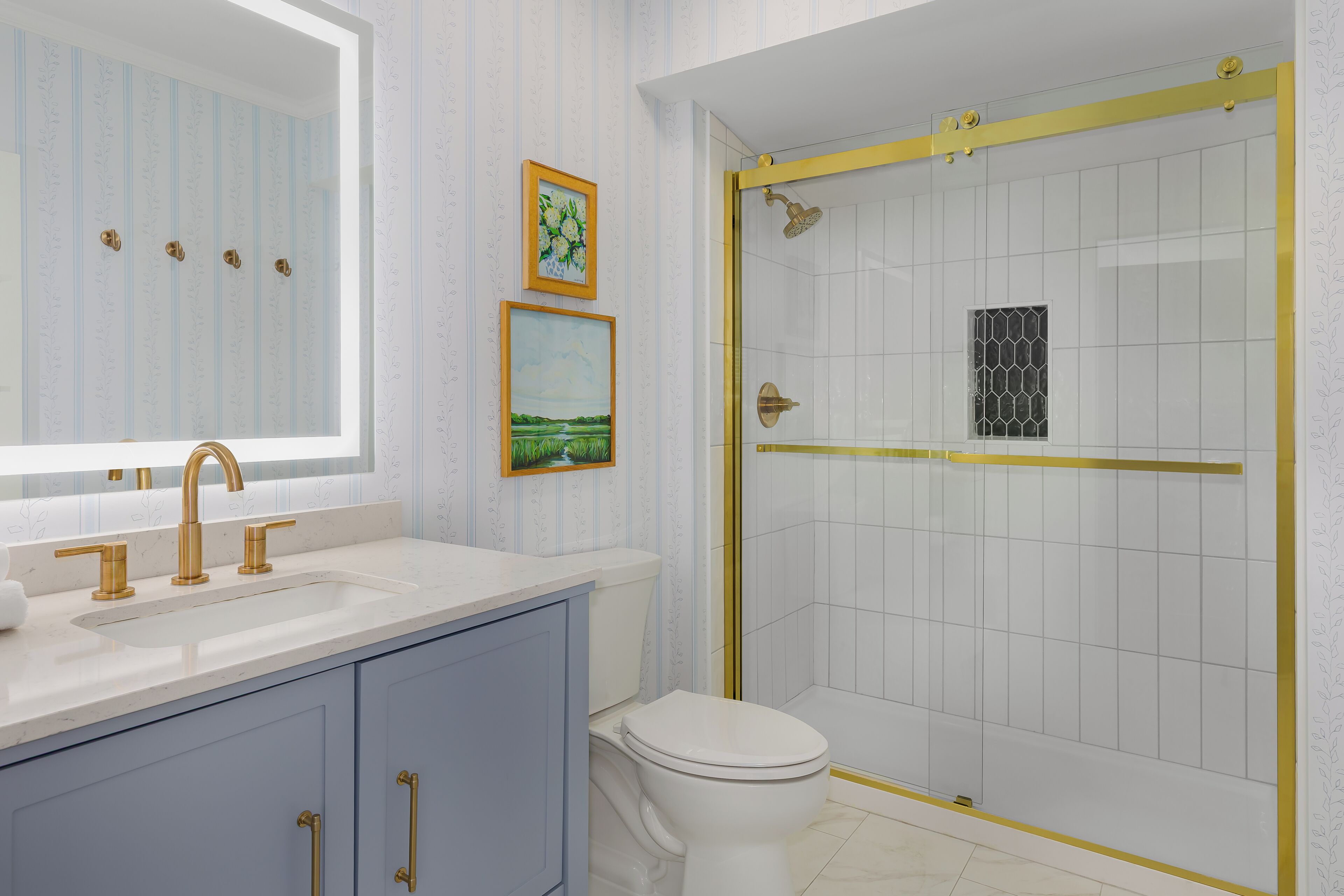 A bathroom with a white sink, gold faucets, a toilet, and a shower with a gold frame.