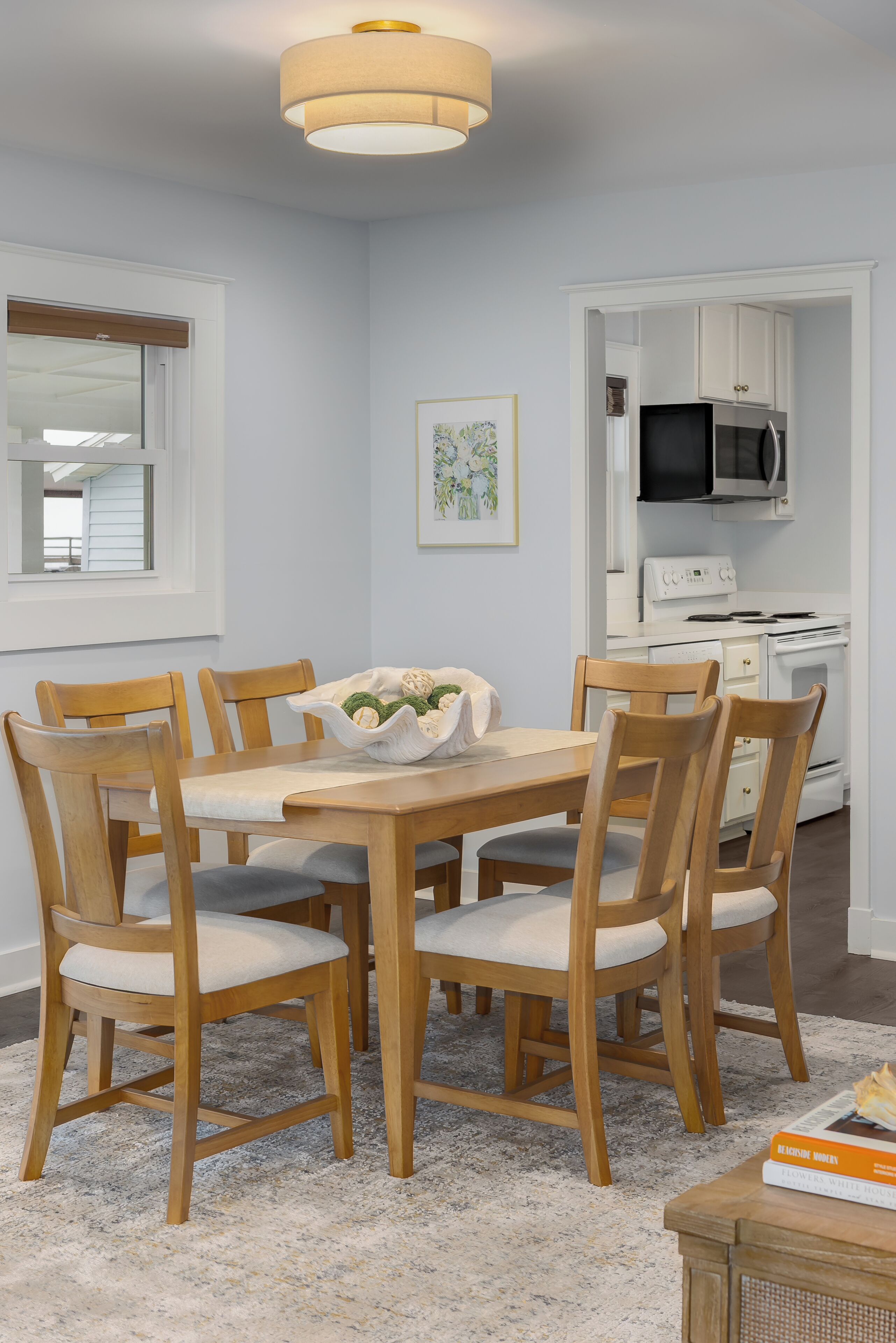 Un espace repas avec une table et des chaises en bois, un lustre et une cuisine en arrière-plan.