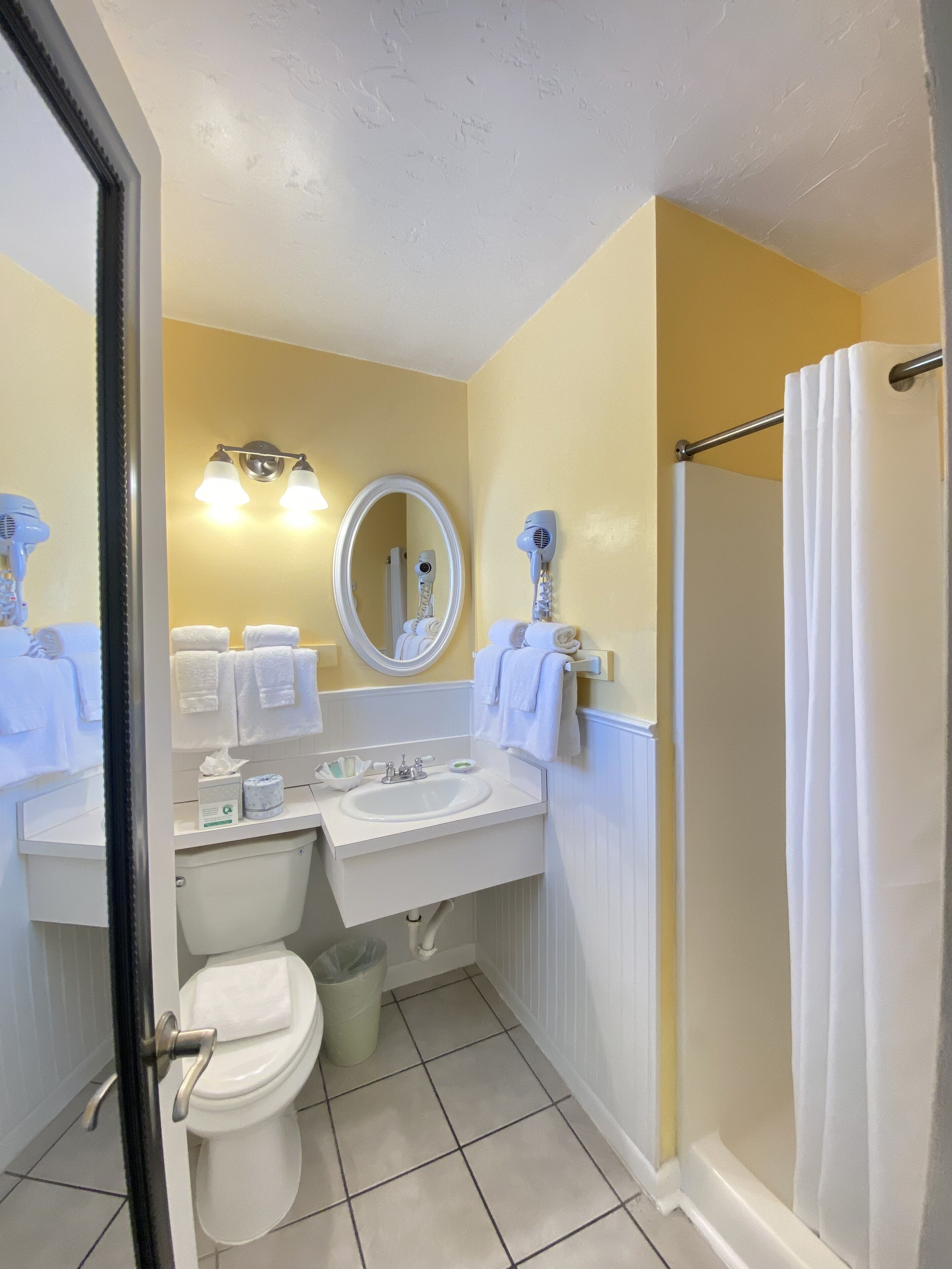 A bathroom with a toilet, sink, and shower. There are towels and a hairdryer on the sink.