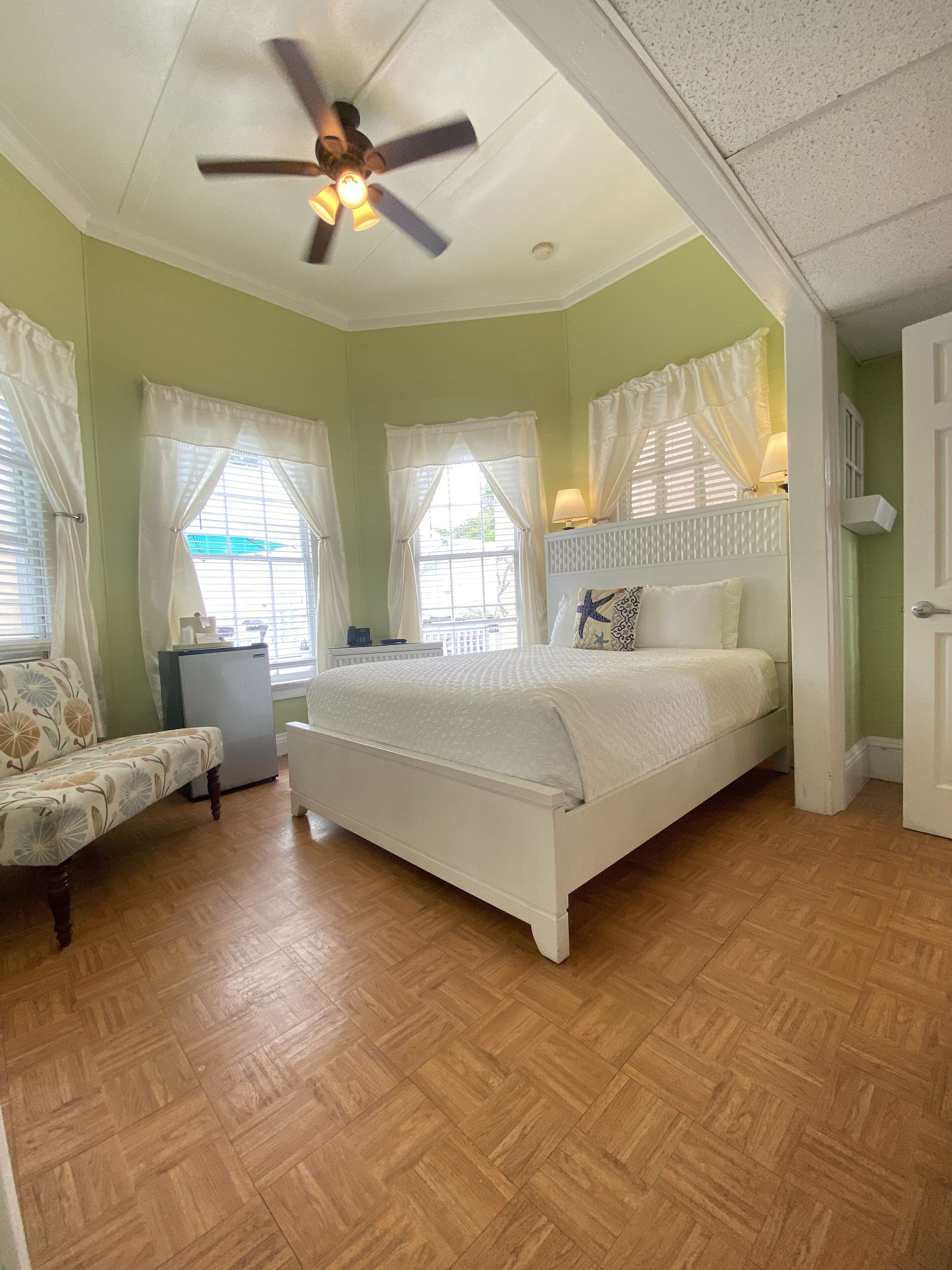 A bedroom with a bed, a ceiling fan, a nightstand, a lamp, and a window with curtains.