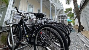 A row of bicycles parked in front of a building with a white balcony and a palm tree.