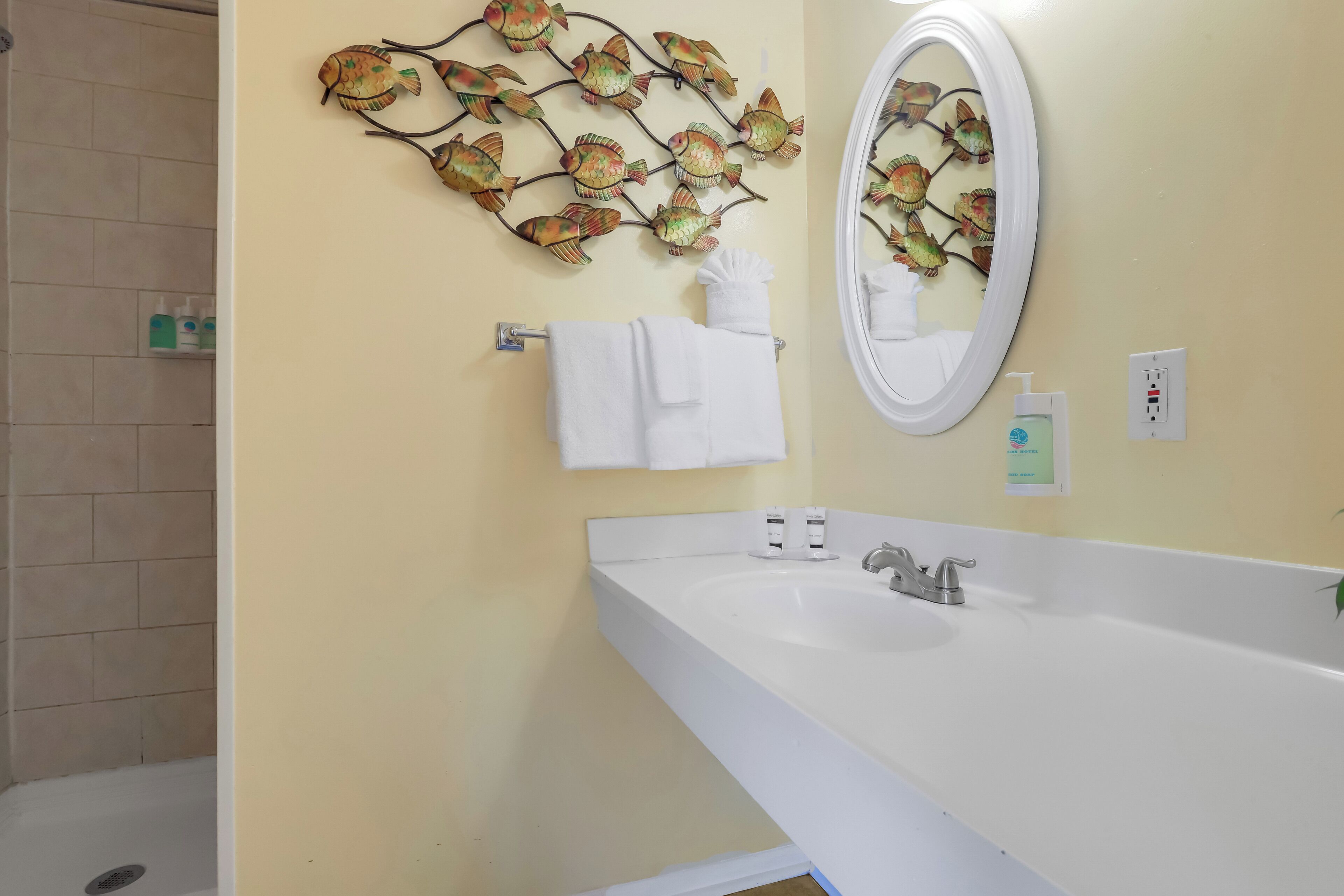 A bathroom with a white sink, a mirror, and a decorative fish wall art piece.