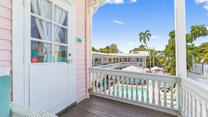 A pink building with a white door, a balcony with a white railing, and a view of a pool area.