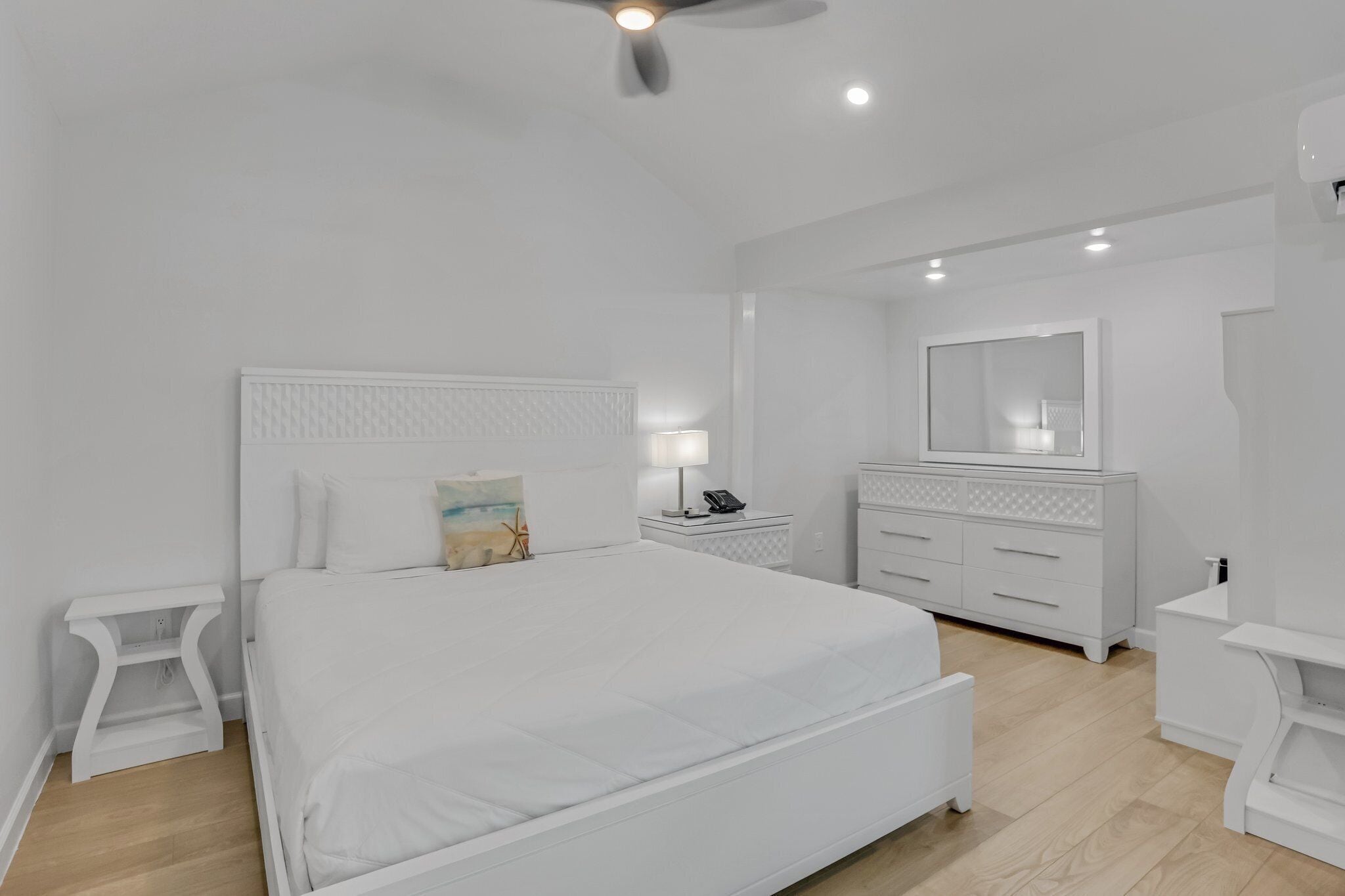 A white bedroom with a bed, bedside tables, a dresser, and a ceiling fan.
