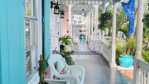 A covered porch with wicker furniture, potted plants, and a sign for the "Office" at the Palm Hotel.