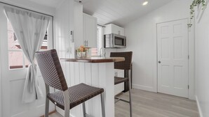 A compact kitchen with white cabinets, a microwave, and a small dining area with two wicker chairs.