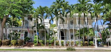 A two-story building with a balcony, surrounded by palm trees and a small garden.