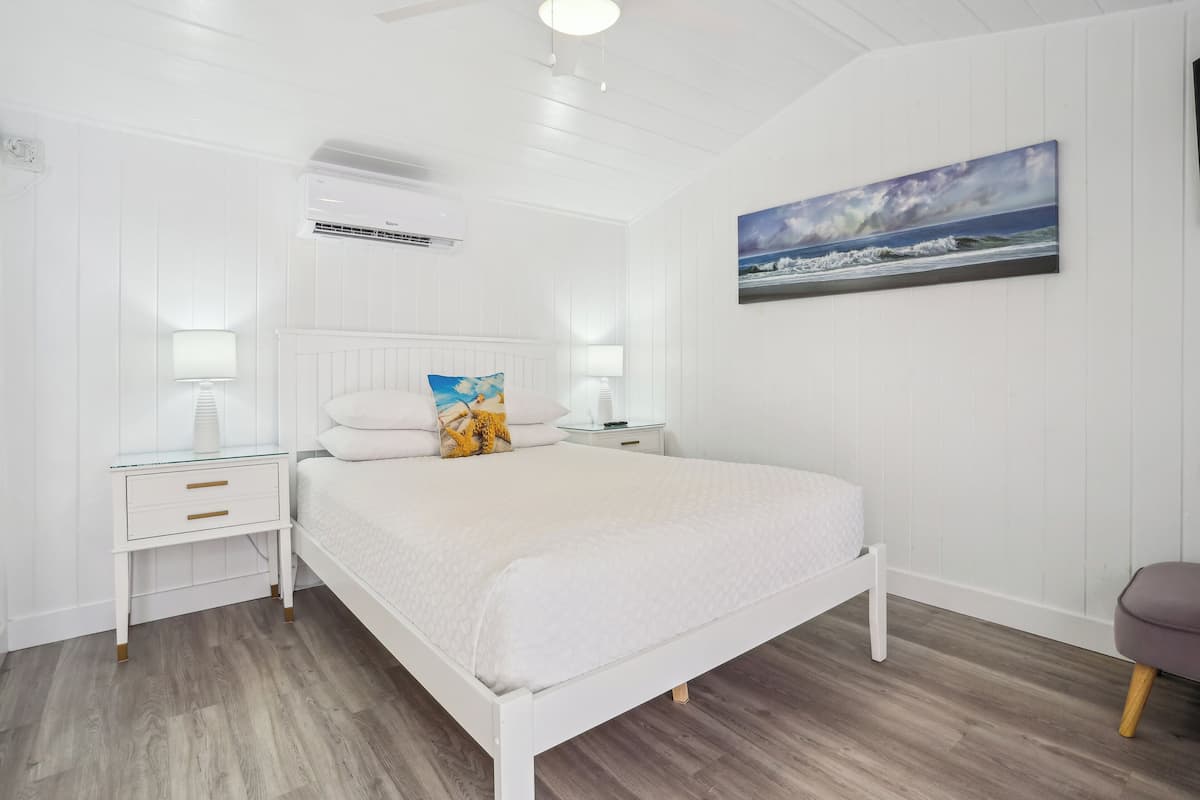 Une chambre à coucher blanche avec un lit, des tables de chevet et un tableau au mur.