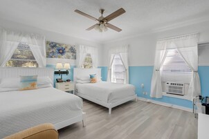 A bedroom with two beds, a ceiling fan, a nightstand with a lamp, and a window with blinds.