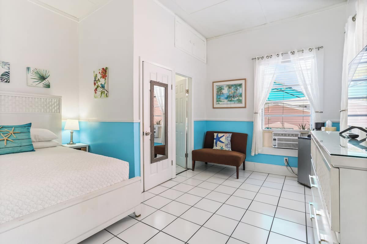 Une chambre d’hôtel avec un lit, une banquette, un bureau et une fenêtre avec des rideaux.