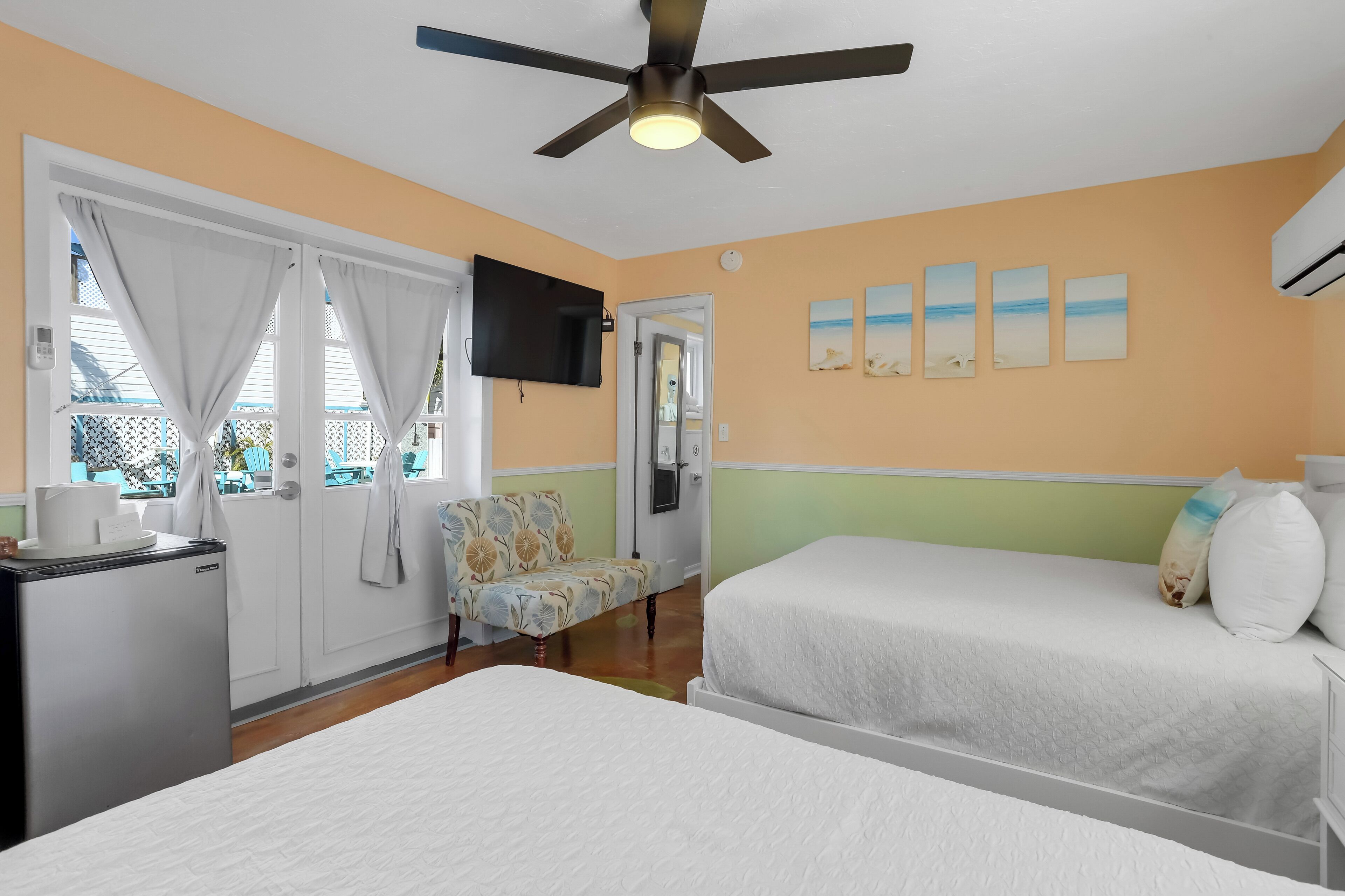 A hotel room with two beds, a ceiling fan, a TV, and a window with curtains.