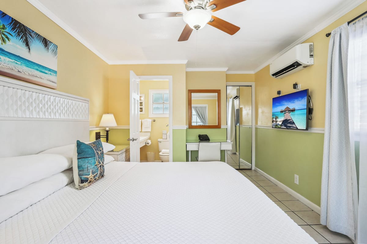 Une chambre d’hôtel équipée d  ’un lit, d’un ventilateur de plafond, d’un appareil de climatisation, d’une salle de bain et d’un téléviseur fixé au mur.