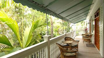 A covered porch with wicker furniture and a white railing, surrounded by lush tropical vegetation.