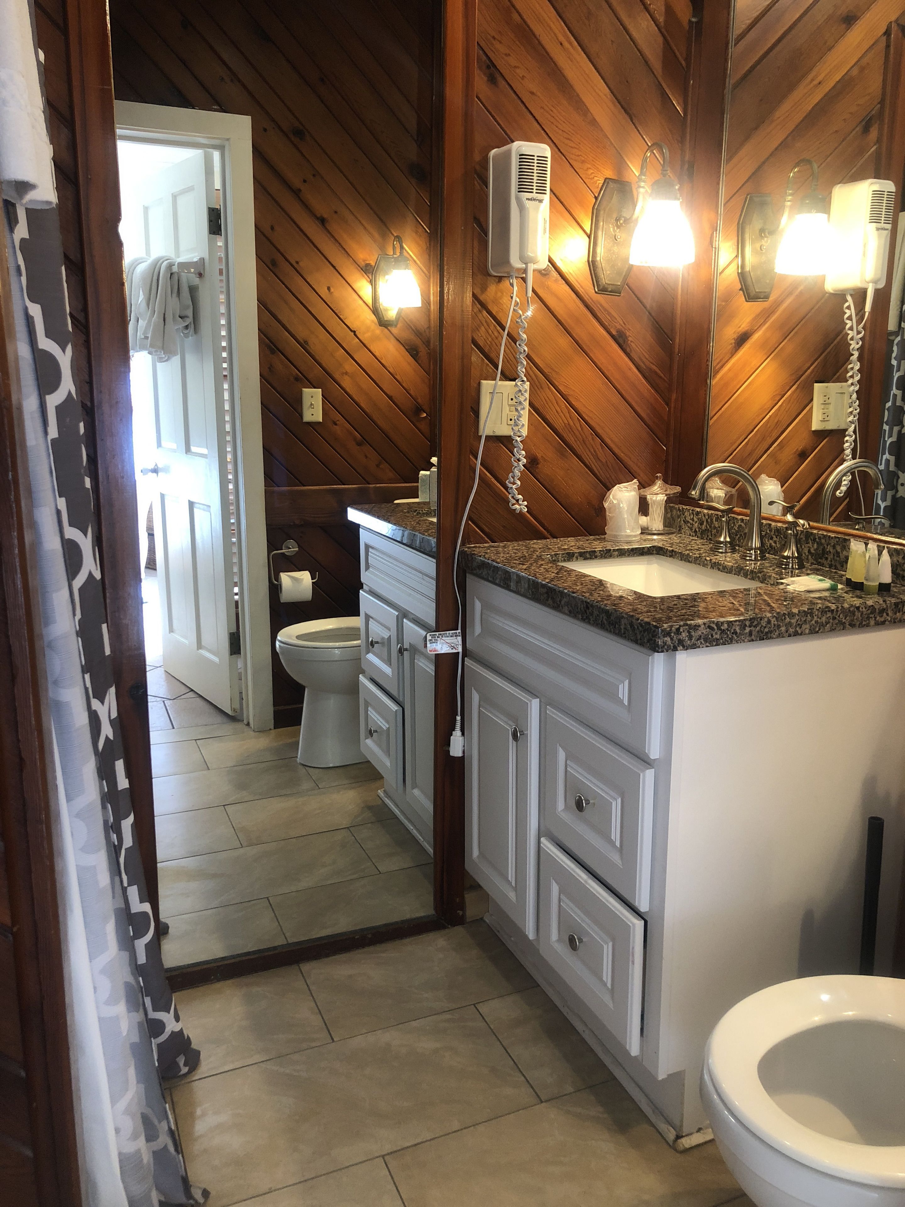 A bathroom with a wooden ceiling, a granite countertop, a white sink, a mirror, and a toilet.