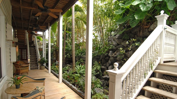A wooden deck with wicker furniture, a white staircase, and a lush garden area.