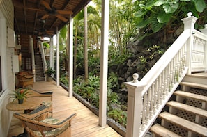 A wooden deck with wicker furniture, a white staircase, and a lush garden area.