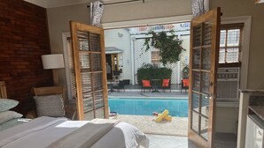 A bedroom with a large bed, a view of a swimming pool, and an open door leading to an outdoor seating area.
