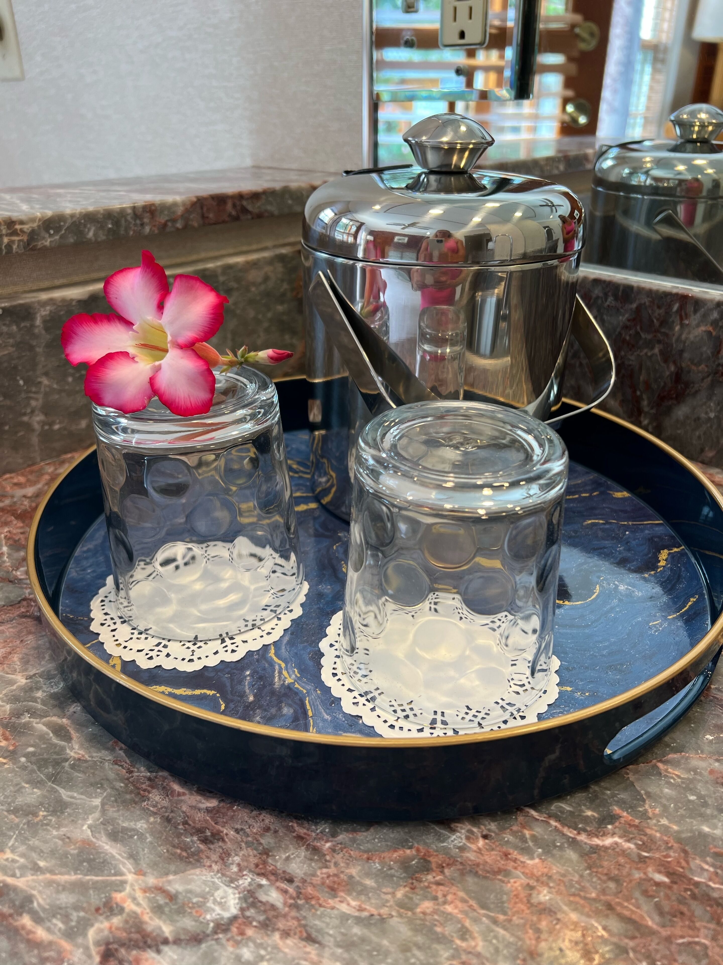 Two glass jars with lace doilies on a blue tray with gold trim, placed on a marble countertop.