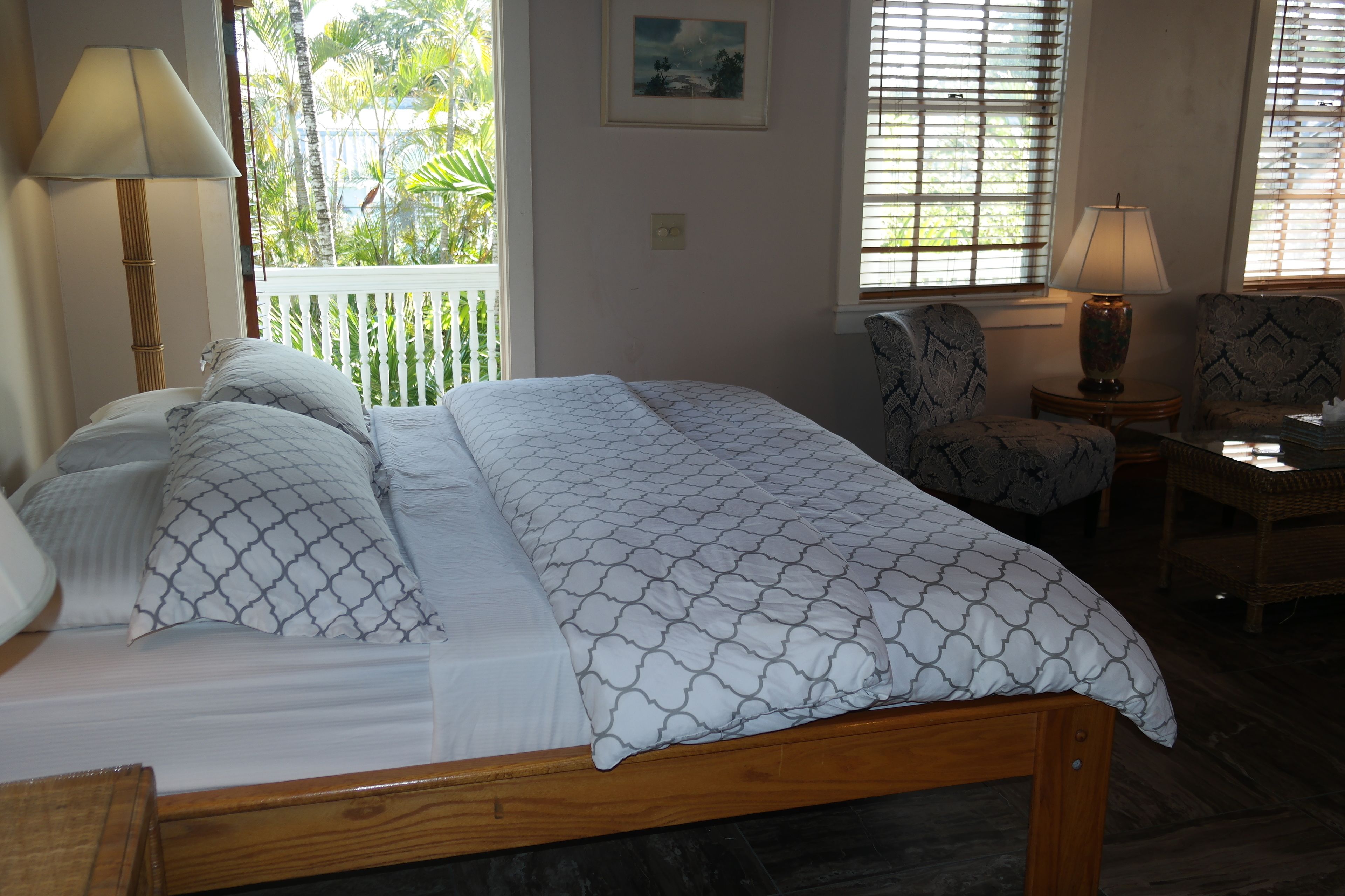 A neatly made bed with patterned bedding, a bedside lamp, a chair, and a small table with a lamp.