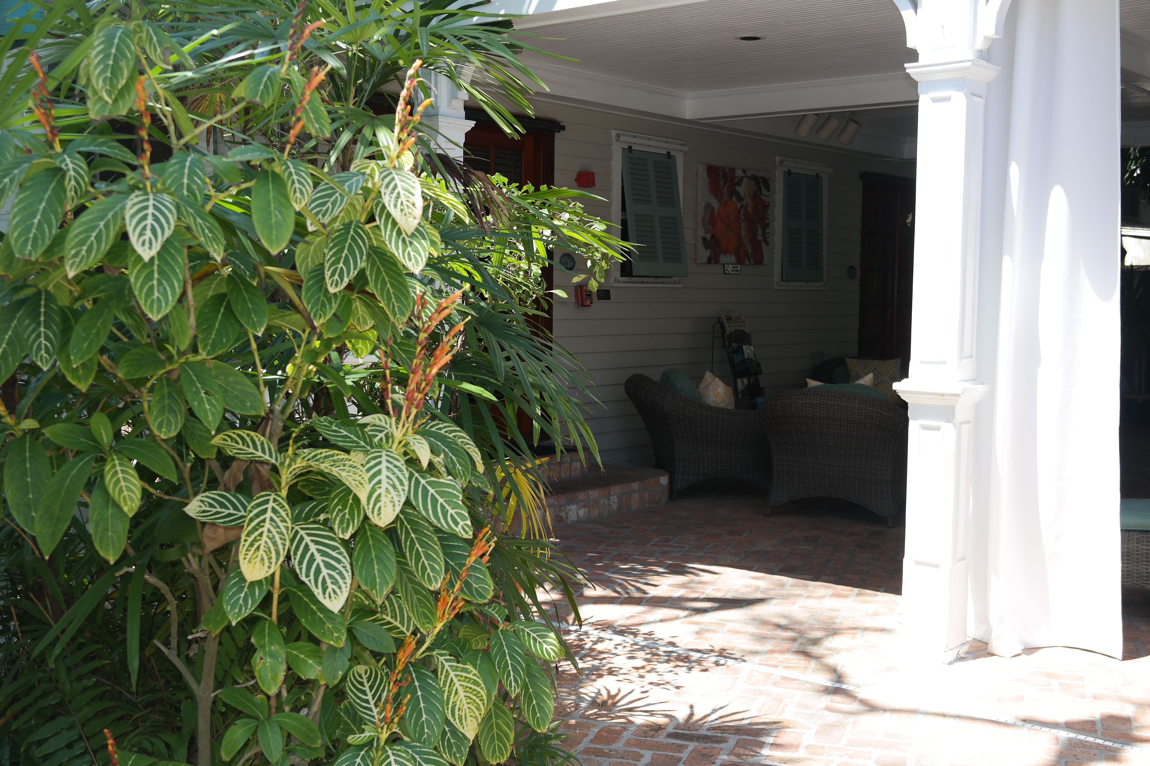 A covered patio area with a brick floor, a white column, and a wicker chair.