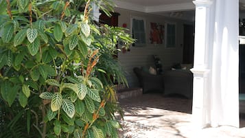 A covered patio area with a brick floor, a white column, and a wicker chair.