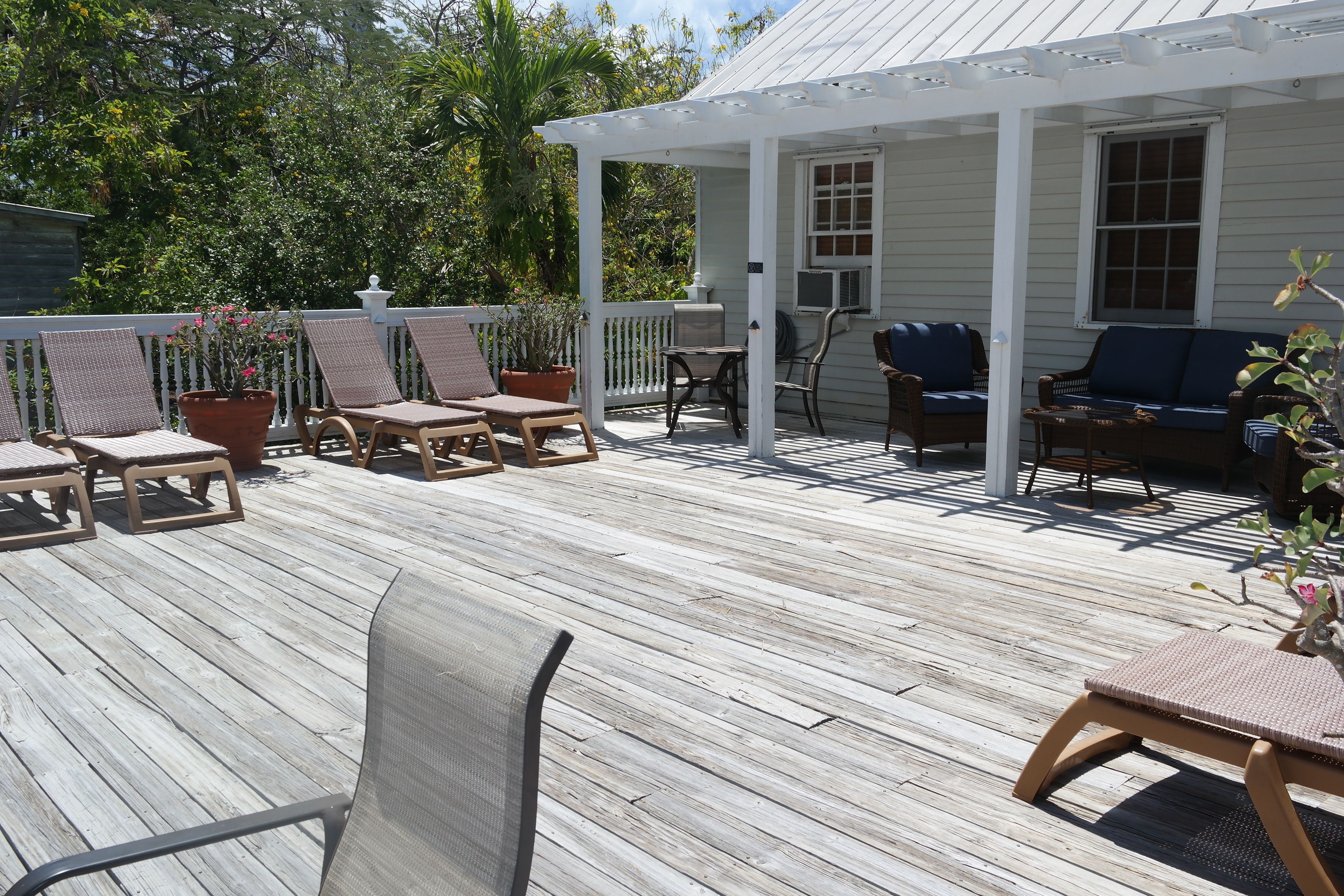 A covered outdoor deck with wooden furniture, including chairs and a table, surrounded by lush greenery.