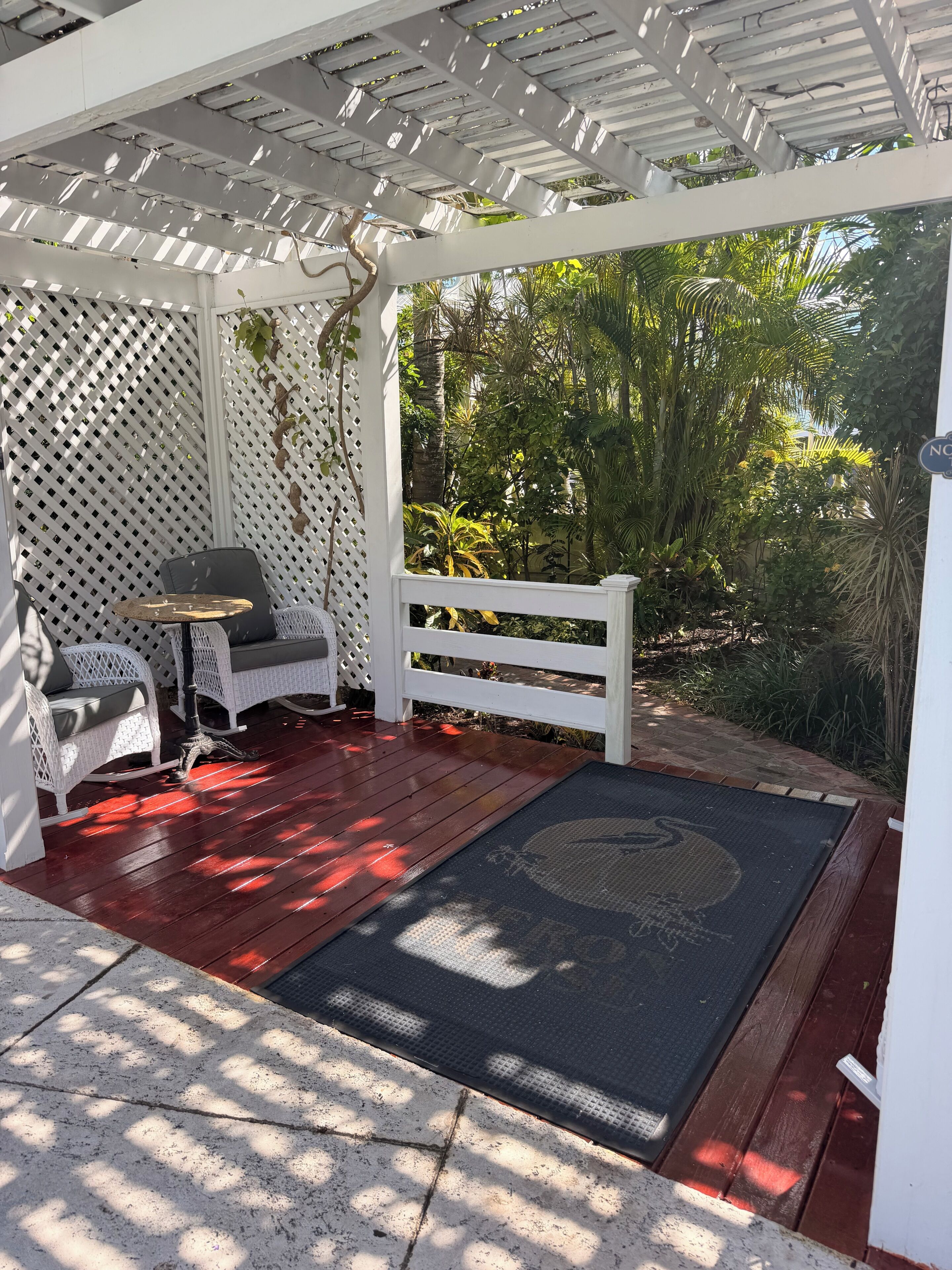 A covered patio with white lattice walls, a wooden deck, and outdoor furniture.