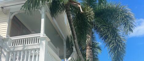 A two-story house with a balcony, surrounded by palm trees and a clear blue sky.