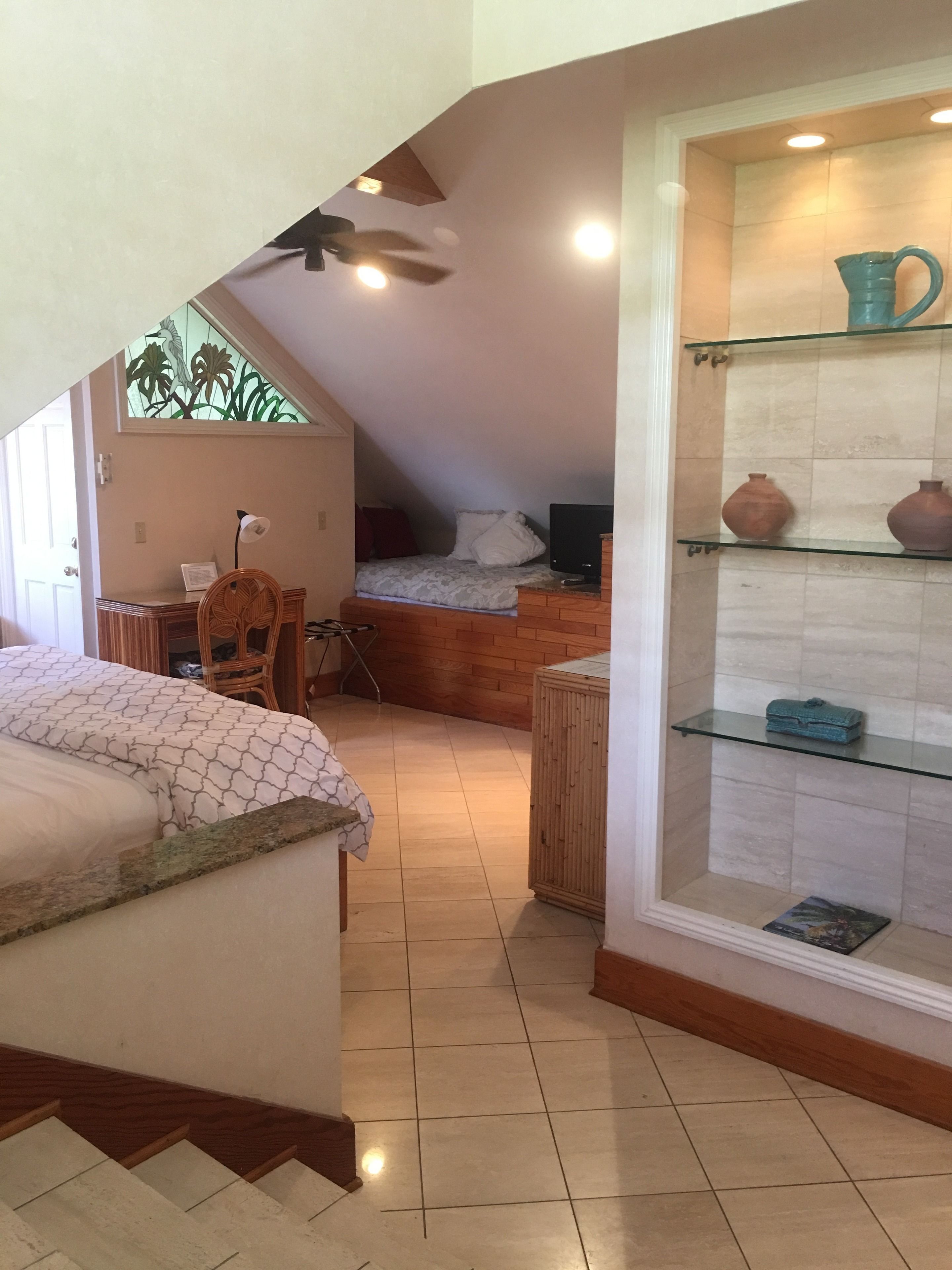 Une chambre à coucher comprenant un lit, un bureau, une chaise, un téléviseur et une étagère avec des objets décoratifs.