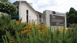 A sign for The University Inn at Emory, surrounded by greenery and yellow flowers. - The University Inn at Emory (Atlanta)
