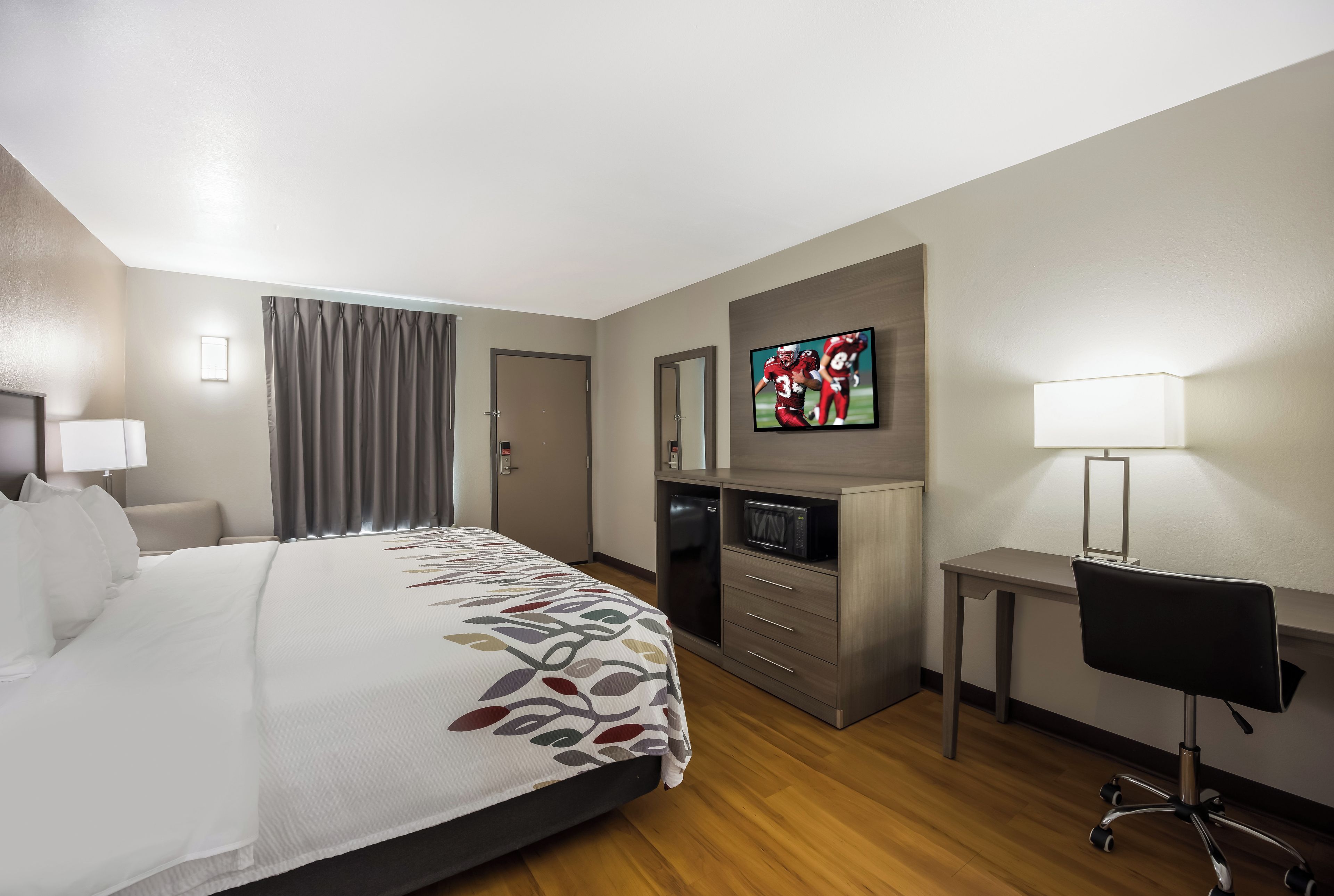 A hotel room with a bed, a desk, a television, and a chair.