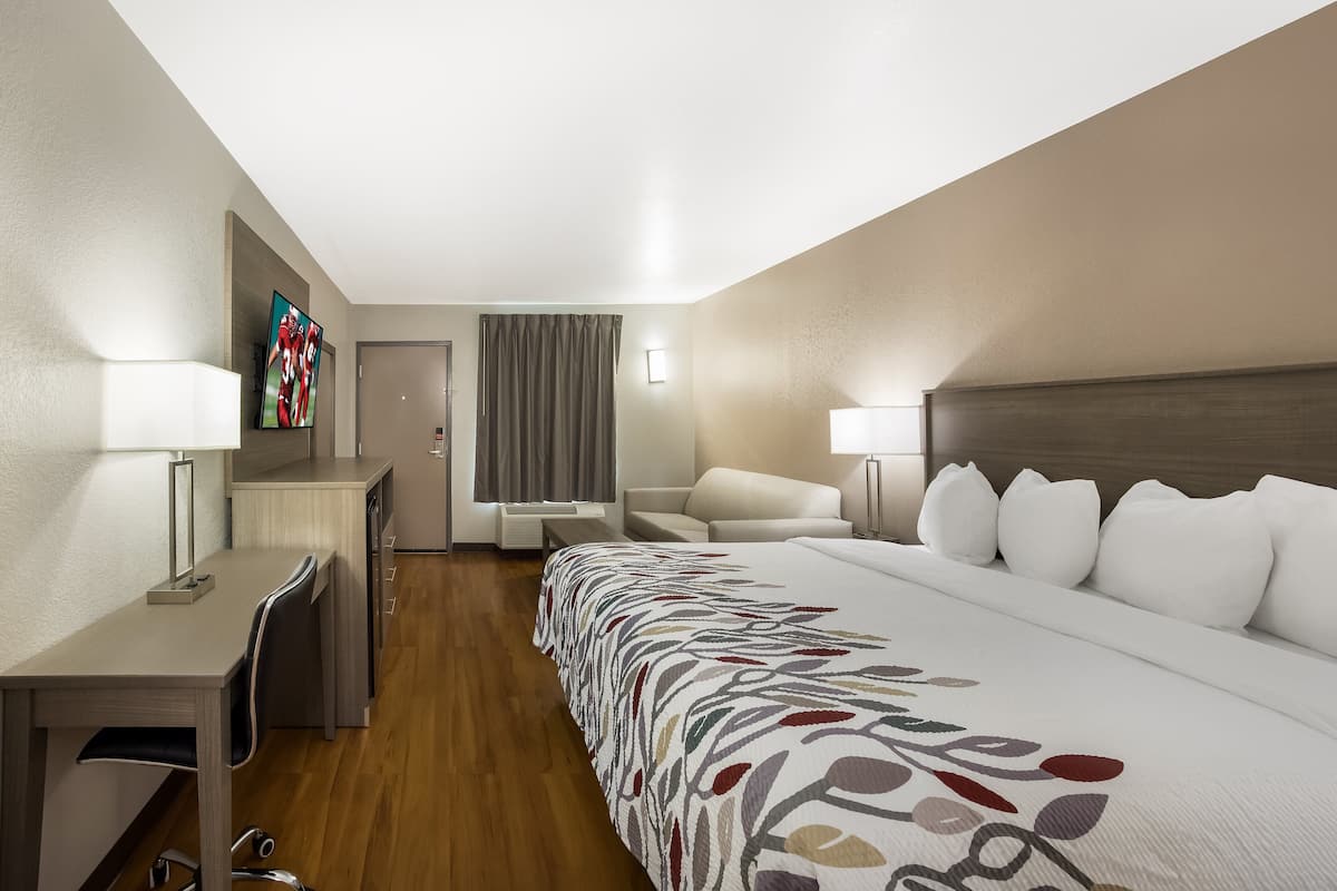 A hotel room with a bed, desk, chair, and a TV on the wall.