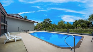A swimming pool with a metal ladder, lounge chairs, and a building with a red roof in the background.