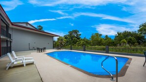 Una piscina con lettini e un tavolo, circondata da una recinzione e alberi.
