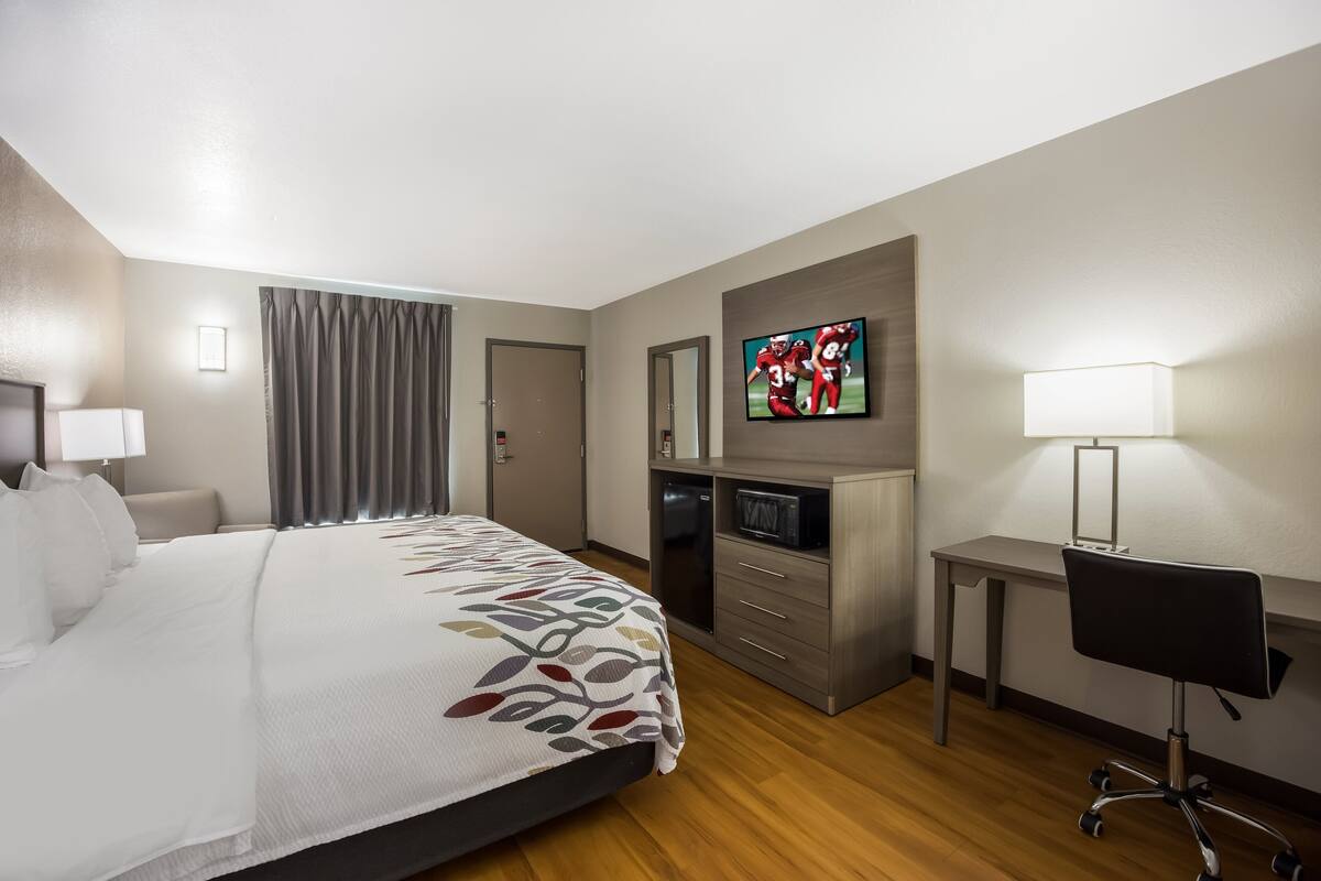 A hotel room with a bed, a desk, a chair, a television, and a lamp.