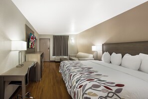 Habitación de hotel con cama, escritorio, silla, televisor y ventana con cortinas.