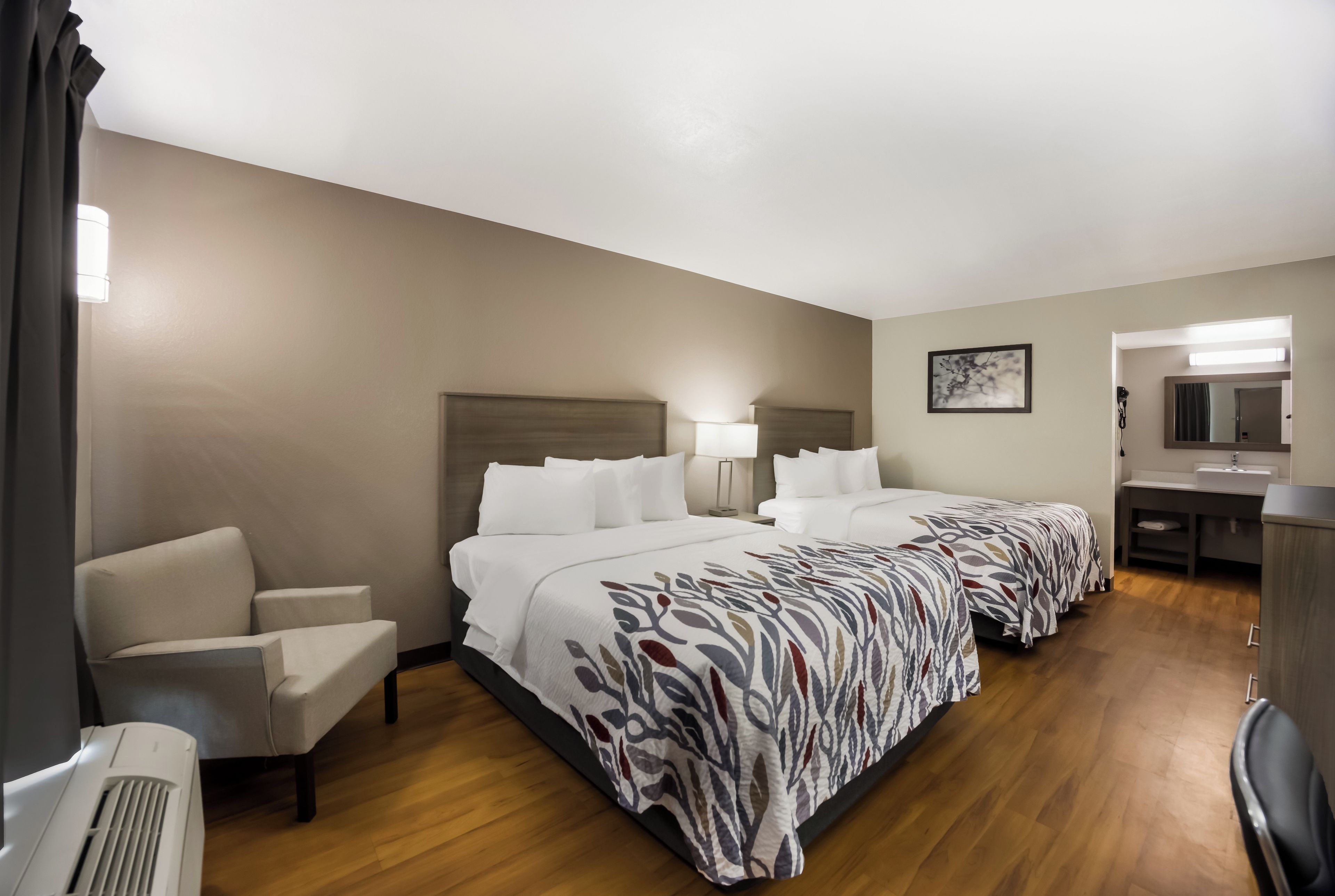 Quarto de hotel com duas camas, uma mesa, uma cadeira e banheiro.