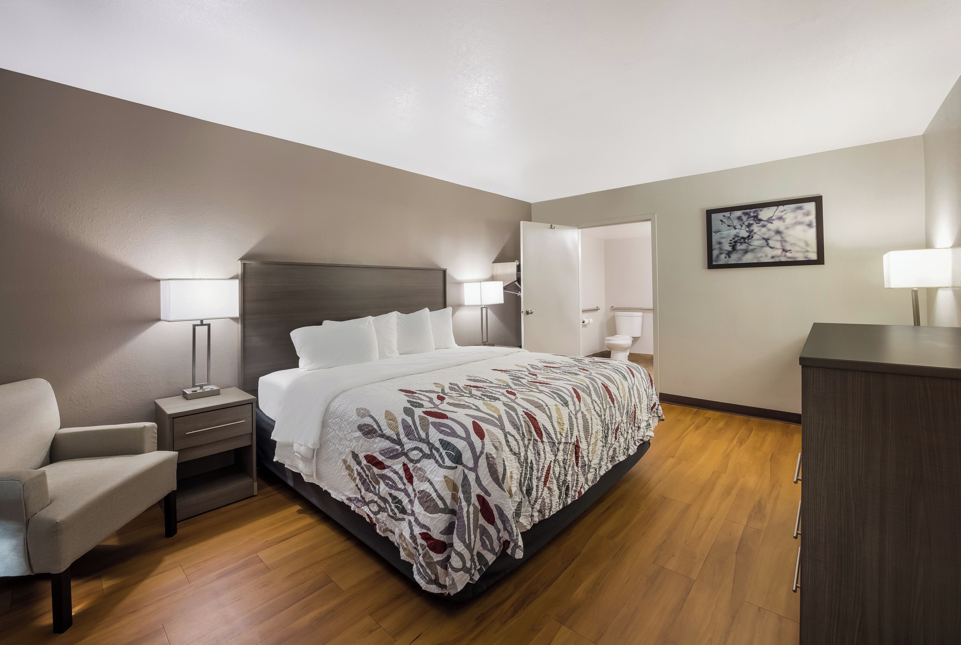 A hotel room with a bed, bedside tables, a chair, a desk, and a wardrobe.
