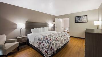 A hotel room with a bed, bedside tables, a chair, a desk, and a wardrobe.