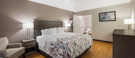 A hotel room with a bed, bedside tables, a chair, a desk, and a wardrobe.