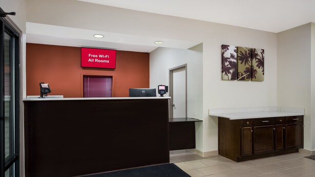 A hotel reception area with a red sign indicating free Wi-Fi, a reception desk, a computer, and a large painting on the wall. - Red Roof Inn & Suites Thomasville (Thomasville)