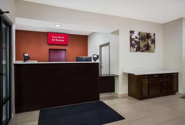 A hotel reception area with a red sign indicating free Wi-Fi, a reception desk, a computer, and a large painting on the wall. - Red Roof Inn & Suites Thomasville (Thomasville)