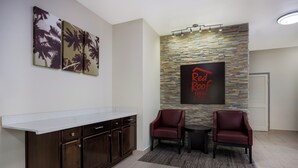 A reception area with a stone wall, a 'Red Roof Inn & Suites' sign, a counter, and two armchairs. - Red Roof Inn & Suites Thomasville (Thomasville)