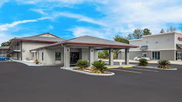 A hotel with a covered entrance, parking lot, and a building with a sign.
