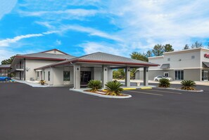 Un hotel con entrada cubierta, estacionamiento y un edificio con letrero.