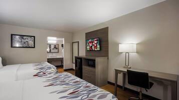 A hotel room with a bed, a desk, a TV, and a bathroom visible through an open door.