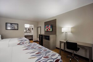 Habitación de hotel con cama, escritorio, televisor y baño visible a través de una puerta abierta.