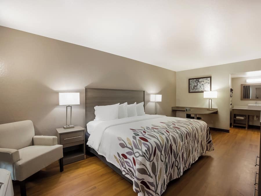 Habitación de hotel con cama, escritorio, silla, mesita de noche, lámpara y baño.