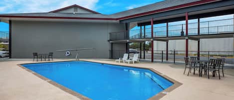 A swimming pool with lounge chairs and tables, a covered patio area, and a view of the sky.